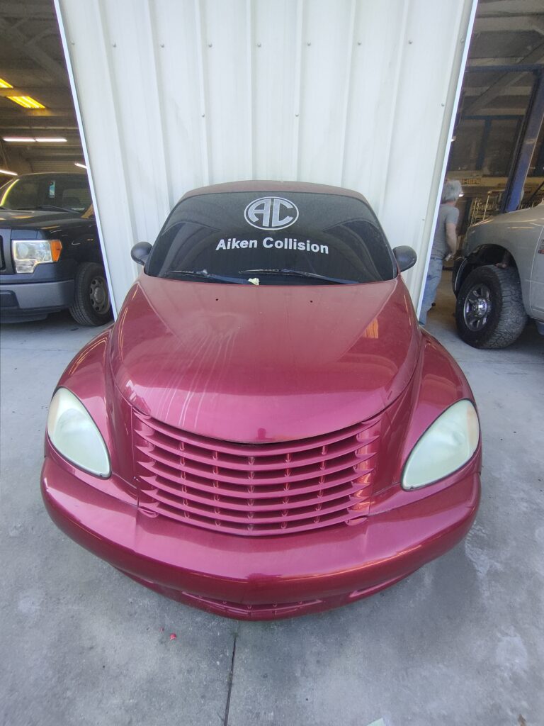 Red vehicle in front of Aiken Collision shop with the AC logo in white